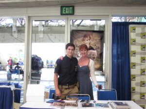An image of Pat and her son standing at her book at a convention.