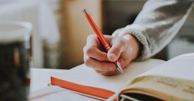 Image of a person holding a pen as they journal.