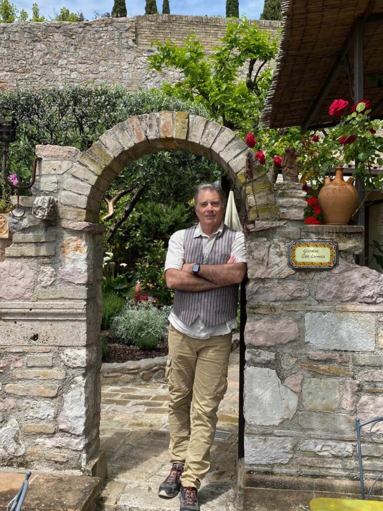 Glenn standing at the stone gate to a coffee shop in Assisi.