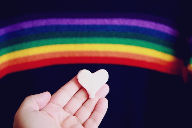 A clay heart being held in front of a rainbow.