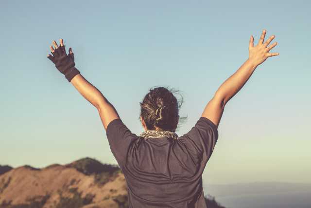 Person raising hands in air, looking out over a cliff.