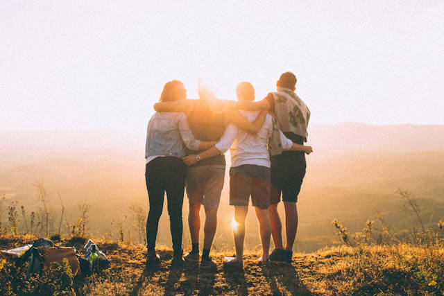 A group of people with their arms around each others' shoulders, staring at the sunrise.
