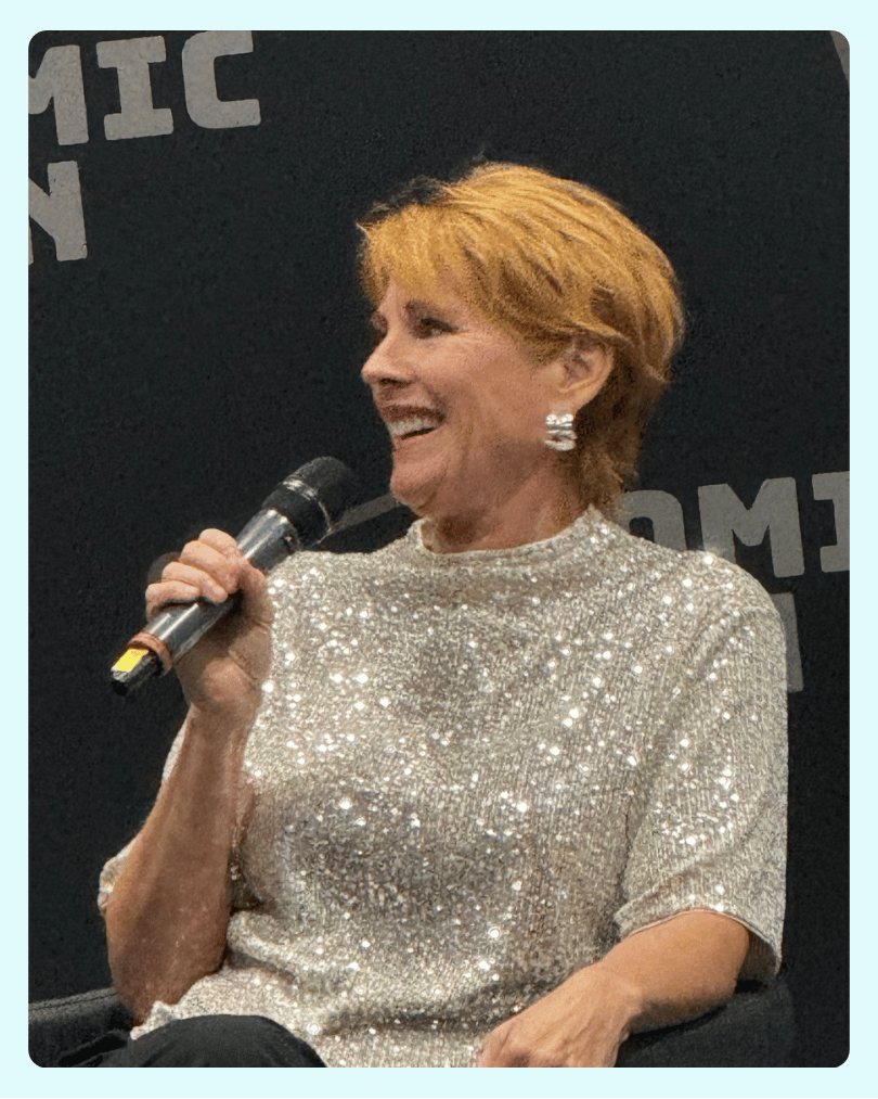 Patricia Tallman on stage at a convention speaking into a microphone and smiling.